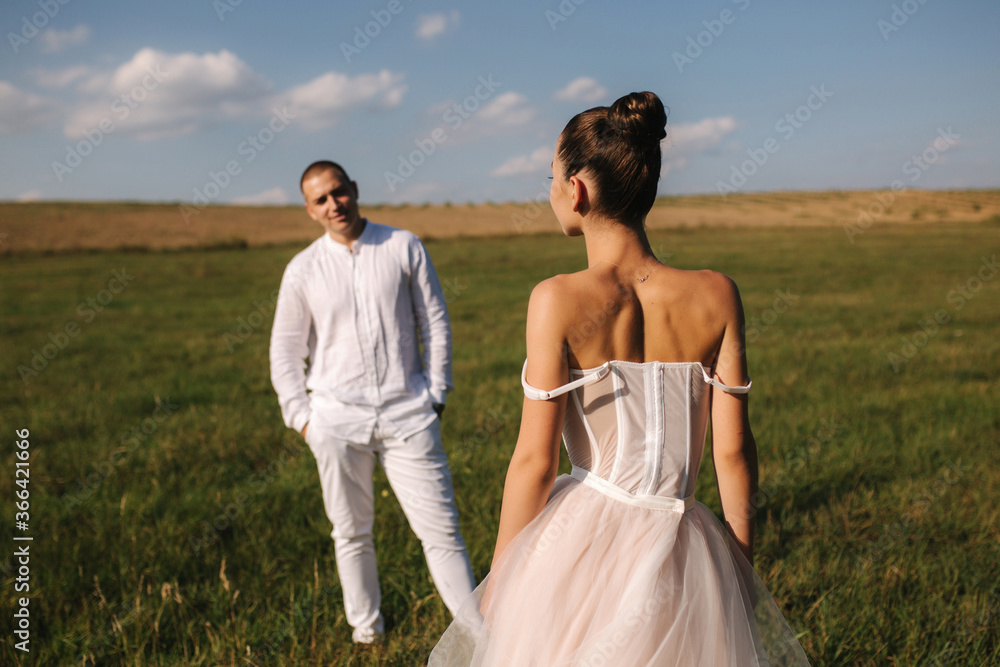 Gorgeous bride with handsome groom walkin in the field after wedding ceremony. Newlyweds posing to photographer