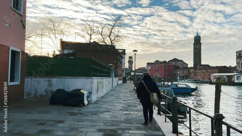 Back View Of A Man Walking At The Pavement Along The Waters In The Island Of Murano In Venice, Italy - dolly shot photo