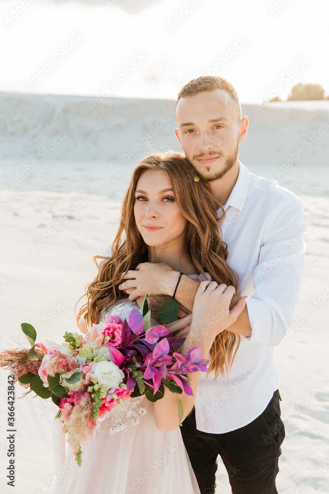 Love Story of a beautiful couple in a pink wedding luxury dress with a bouquet in the Sahara desert, sand, dunes Love Story of a beautiful couple in a pink wedding luxury dress with a bouquet in the Sahara desert, sand, dunes