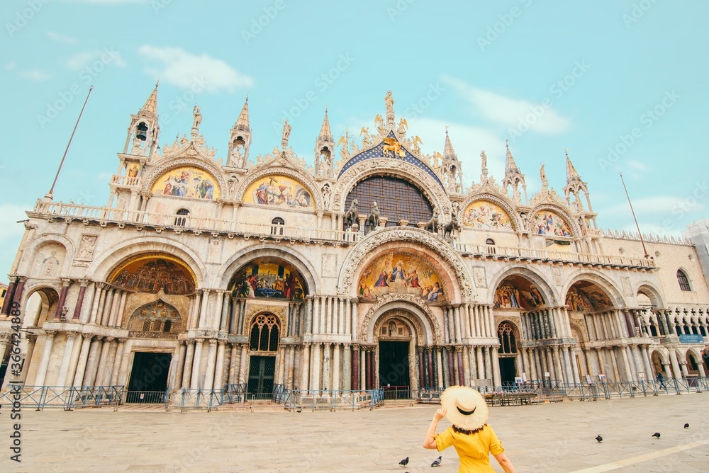 woman in yellow sundress with straw hat walking to saint mark basilica