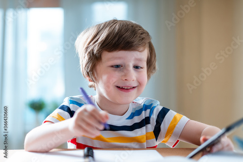 Back to school. Distance learning online education. Caucasian smile kid boy studying at home with smartphone and doing school homework. Smiling child siting at table with cell phone