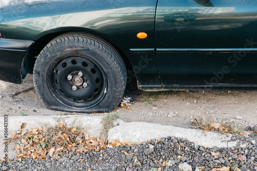 Green car with a punctured wheel in the open air. Damaged flat tire of a car.