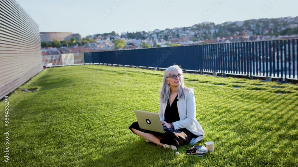 Old businesswoman working outdoors in city, using laptop. Old businesswoman working outdoors in city, using laptop.