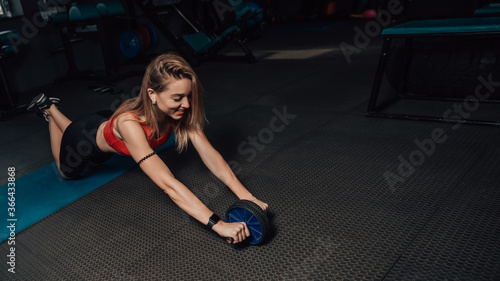 Close up portrait of beautiful woman doing exercises for abdominal muscles. Healthy lifestyle concept. Gym interior. Copy space. Roller slide on mat. 