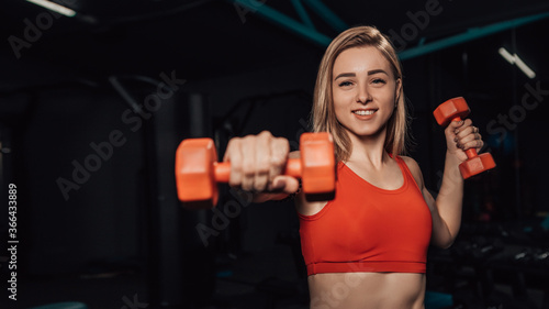 Young attractive girl doing exercise with dumbbells to be strong and energetic. Health care concept with copy space. Female in sportwear give motivation. 