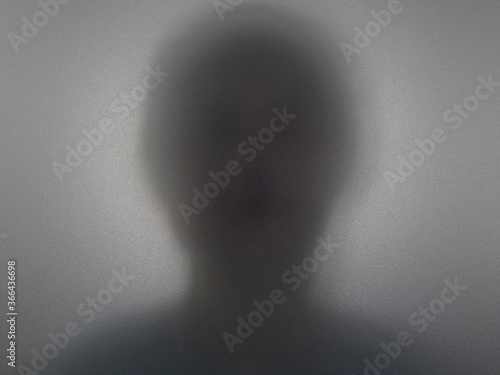 Blurry dark silhouette of a woman figure behind a smoked glass.