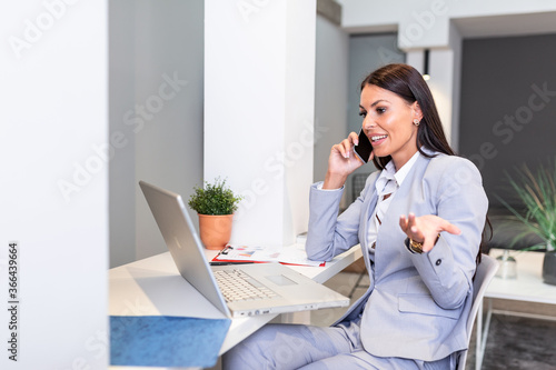 Business woman usingmobile phone, looking at laptop screen, chatting, reading or writing email, sitting in home office, female student doing homework, working on research project online © Graphicroyalty