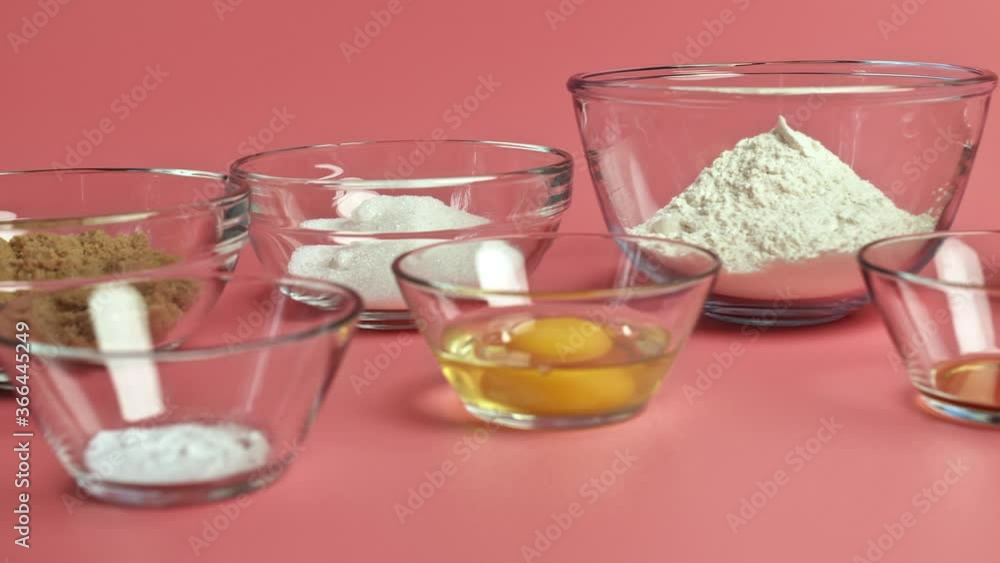 Chocolate Chip Cookies ingredients in glass bowls on a pink background: brown sugar, white sugar, chocolate chips, eggs, flour, butter, vanilla extract, baking soda, salt in 4K. Chocolate Chip Cookies ingredients in glass bowls on a pink background: brown sugar, white sugar, chocolate chips, eggs, flour, butter, vanilla extract, baking soda, salt in 4K.