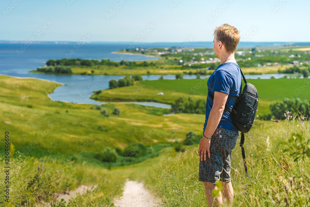 Portrait of a blond man against the background of endless green meadows and fields with a river, panorama of a mountain landscape