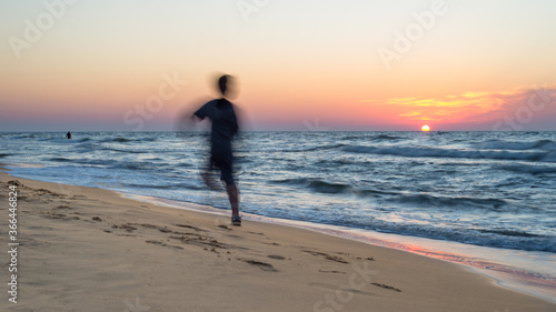 Beautiful sunset at the sea with rough waves on a hot, summer evening, visible shadow of a running person. 