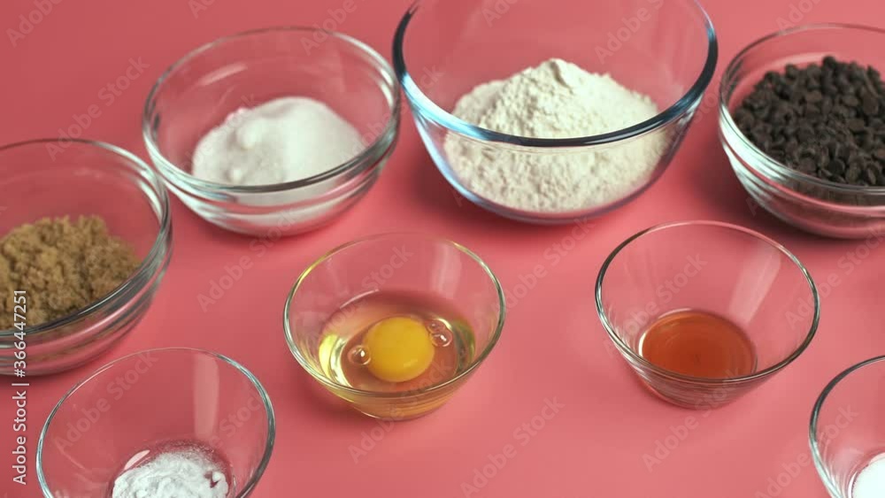 Chocolate Chip Cookies ingredients in glass bowls on a pink background: brown sugar, white sugar, chocolate chips, eggs, flour, butter, vanilla extract, baking soda, salt in 4K. Chocolate Chip Cookies ingredients in glass bowls on a pink background: brown sugar, white sugar, chocolate chips, eggs, flour, butter, vanilla extract, baking soda, salt in 4K.