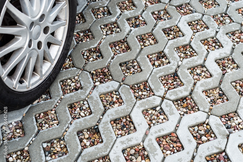 Alloy car wheel on wet openwork concrete pavement filled with colorful pebbles.