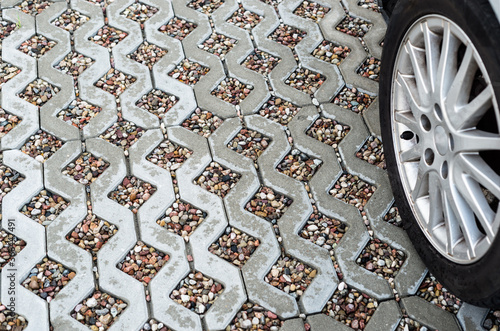 Alloy car wheel on wet openwork concrete pavement filled with colorful pebbles.