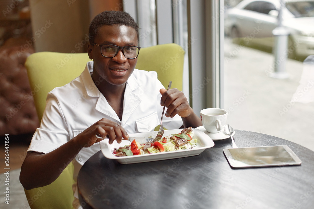 Black man in a cafe. Guy eating a salad. Man in a white shirt. Black man in a cafe. Guy eating a salad. Man in a white shirt.
