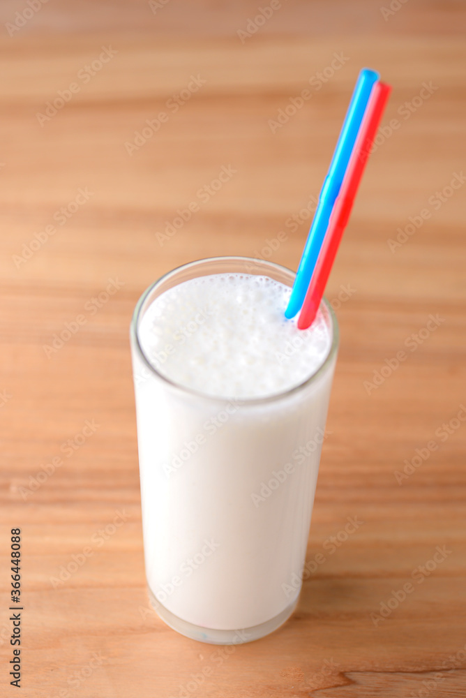 Vanilla milkshake in a tall galss with two plastic straws on light rustic wooden table. Vanilla milkshake in a tall galss with two plastic straws on light rustic wooden table.