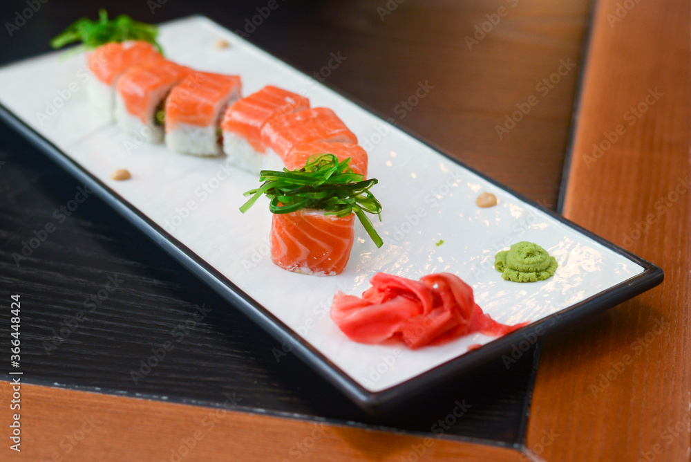 Salmon sushi rolls served on a white plate with ginger and wasabi and soy sauce in a restaurant table. Japanese cuisine. Salmon sushi rolls served on a white plate with ginger and wasabi and soy sauce in a restaurant table. Japanese cuisine.