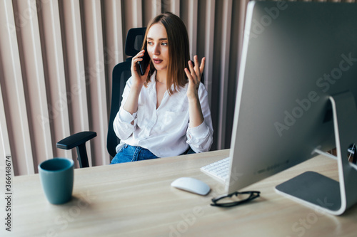 Young woman working on laptop at office while talking on phone