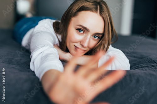 Thoughtful casual woman in white pajamas lying on her bed in a bright bedroom