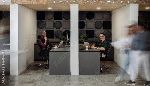 Bilde på lerret Two businessmen working in cubicles in a busy modern coworking office