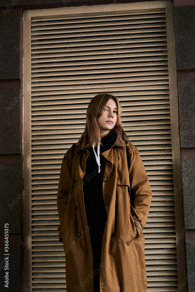 Portrait of beautiful bright model girl with long hair and nude makeup in orange cape and black hoodie stands in city on the street with ventilation grill background. Lifestyle and fashion concept. Portrait of beautiful bright model girl with long hair and nude makeup in orange cape and black hoodie stands in city on the street with ventilation grill background. Lifestyle and fashion concept.