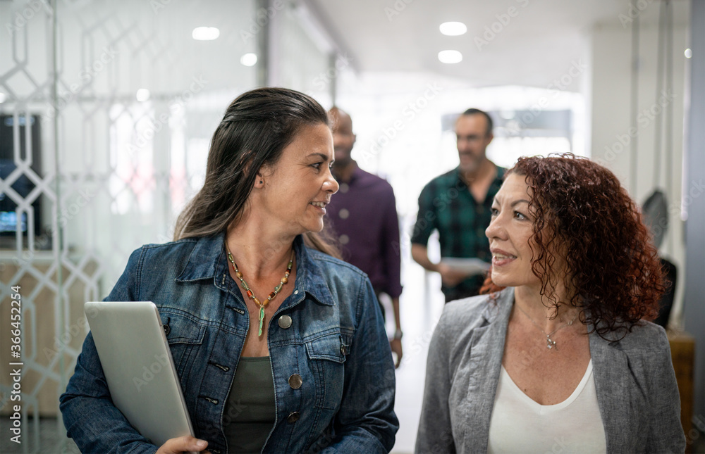 Smiling businesswoman talking while walking together down an office hallway Smiling businesswoman talking while walking together down an office hallway