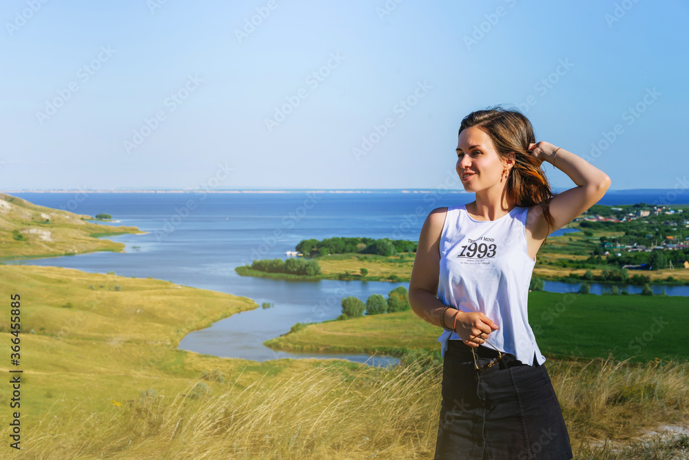 Portrait of a brunette woman against the background of endless green meadows and fields with a river, panorama of a mountain landscape