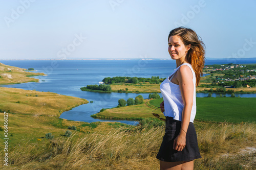 Portrait of a brunette woman against the background of endless green meadows and fields with a river, panorama of a mountain landscape