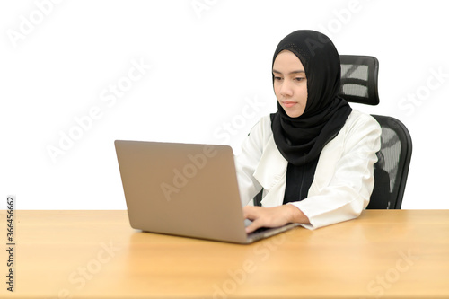 Muslim women sitting at the table in the studio. She is typing text on the laptop keyboard. White background.