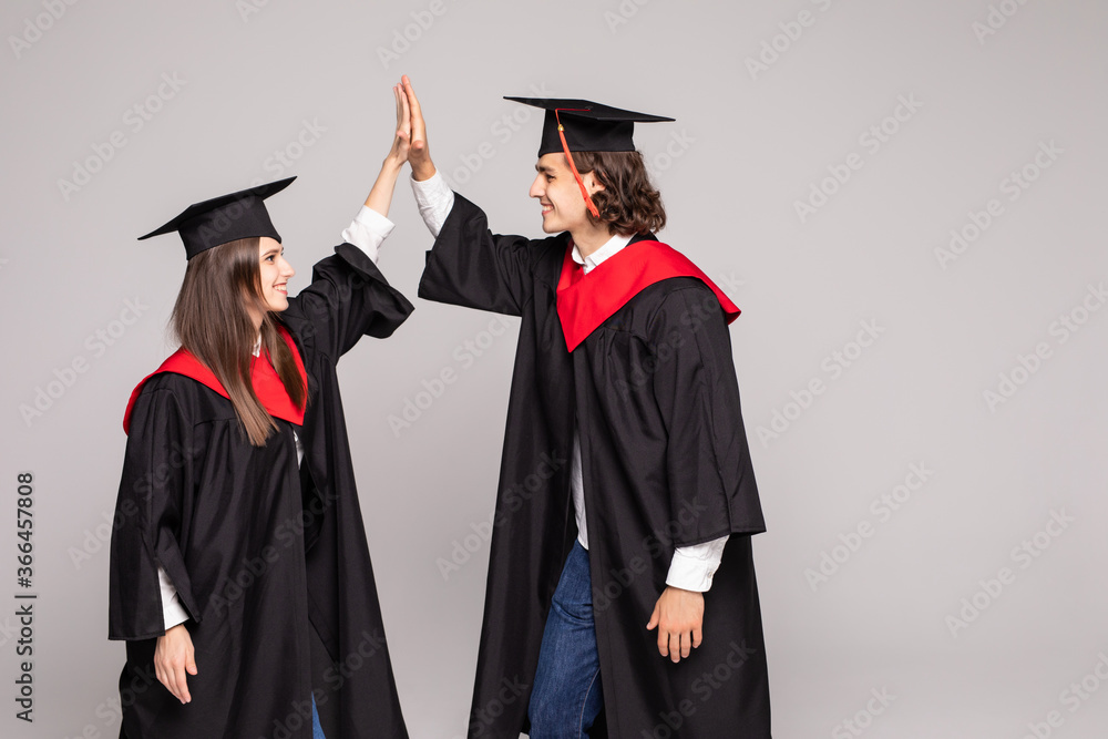 Two happy college graduates giving high five smiling after receiving diplomas over white background. Two happy college graduates giving high five smiling after receiving diplomas over white background.