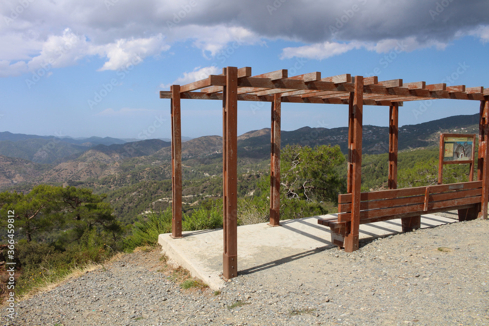 A bench for rest with a sunshade in the Troodos mountains against a blue sky with clouds. Cyprus.