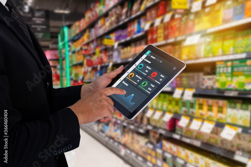 iot smart retail in the futuristic concept, the retailer hold the tablet and use augmented reality technology monitor data of out of shelve, price, planogram, campaign of compliance in the real time photo