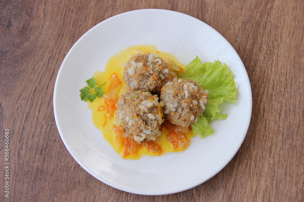 Meatballs with rice and carrots on a white plate and dark wooden boards Meatballs with rice and carrots on a white plate and dark wooden boards