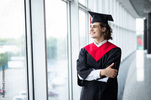 Young man in graduation cap smiling and gesturing in university