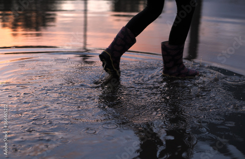 Little girl in rubber shoes stands in puddle. Happy childhood concept.