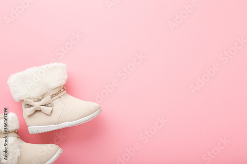 Beige leather warm baby boots with fluffy edges on light pink floor background. Pastel color. Empty place for text. Closeup. Top down view.