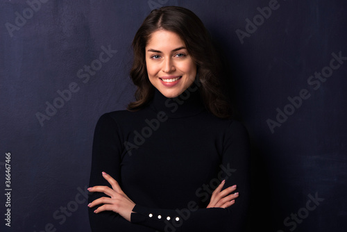 Attractive young woman looking at camera and smiling while standing at dark background