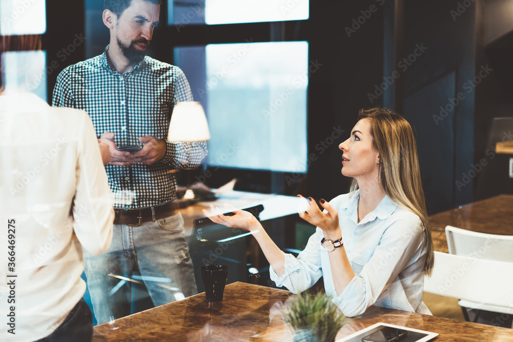 Female gesturing while explaining information to colleague teamworking on business plan together, male employee holding mobile phone for chatting while asking consultancy of skilled coworker . Female gesturing while explaining information to colleague teamworking on business plan together, male employee holding mobile phone for chatting while asking consultancy of skilled coworker .