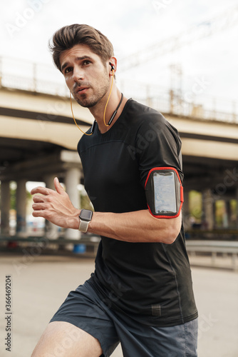 Image of athletic caucasin sportsman using earphones while running