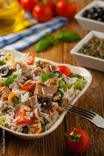Italian tuna salad with rice, olives and capers. Front view. Natural wooden background.