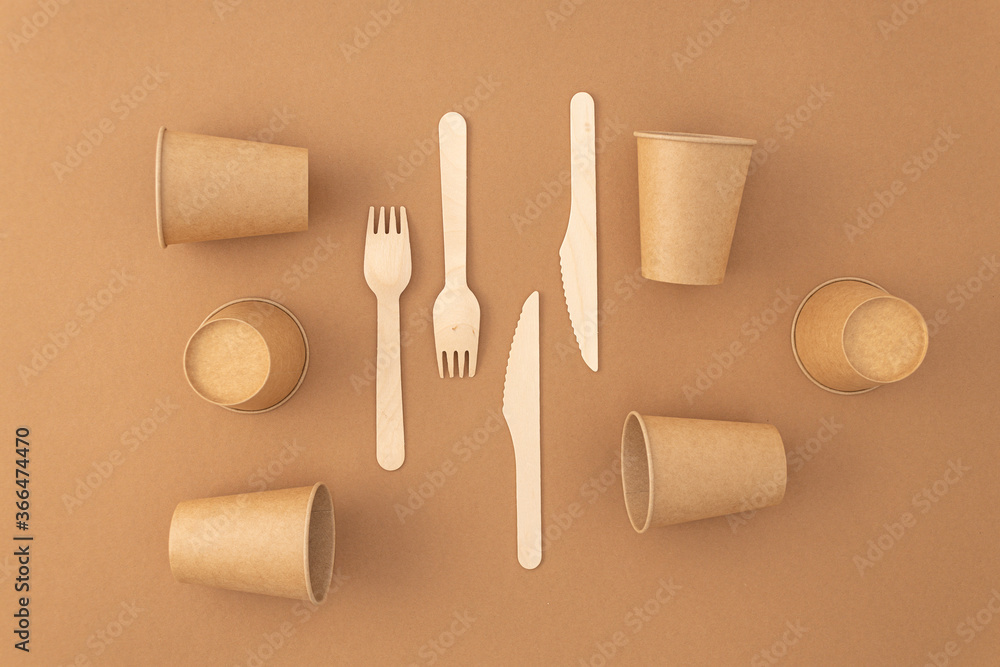 Naklejka premium Disposable paper cups with wooden forks and knives on beige background. Zero waste, plastic free concept