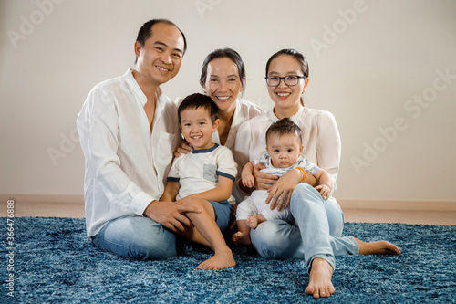 happy asian family hugging together white background sitting on blue carpet rug on floor, multi generation smiling east asian family portrait, mum, dad, two kids and grandma