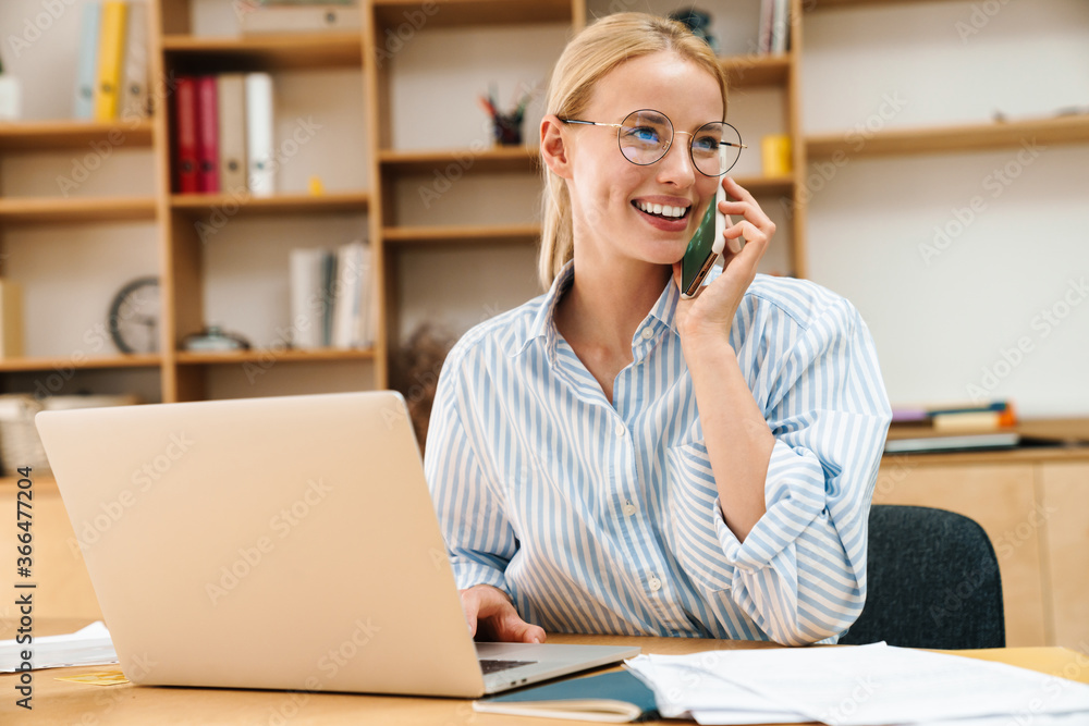 Image of businesswoman talking on cellphone while working with laptop Image of businesswoman talking on cellphone while working with laptop
