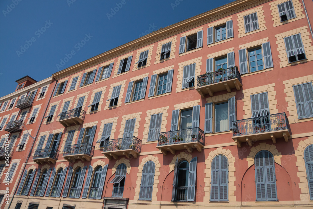 Traditional colorful painted building with blue shutters and balconies under a clear blue sky in Nice, France