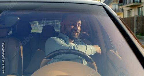 Close up of handsome young man opening car door, gettinng behind wheel, pinches seat belt and touching new luxury car and start to drive happily smiling. Lifestyle, road, car, driver concept. photo