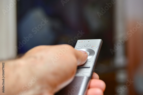 A man holds a remote control in his hand and switches channels to watch TV. Remote control of household appliances.