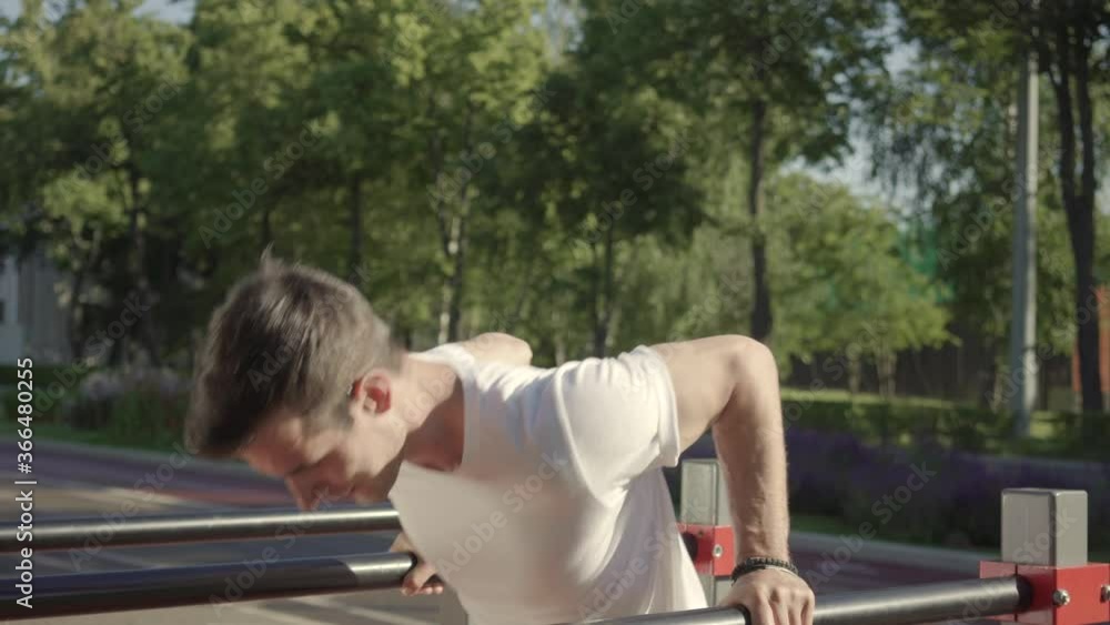 Athletic young man doing parallel bar dips on urban sports ground Athletic young man doing parallel bar dips on urban sports ground
