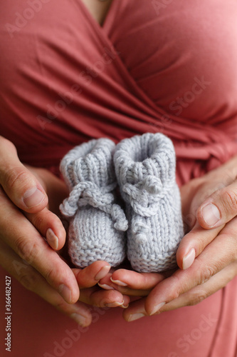 A man father holds the hands of a woman's mother in his arms against the background of a pregnant belly. Parents hold little booties in their hands