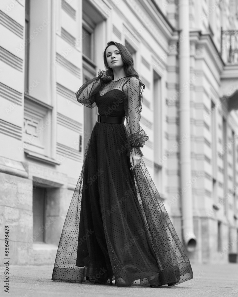 Elegant woman wearing long blue evening dress. Pretty lady posing outdoors. Fashionable stylish model. Fashion outdoor portrait. Female with long wavy hair standing at city street Elegant woman wearing long blue evening dress. Pretty lady posing outdoors. Fashionable stylish model. Fashion outdoor portrait. Female with long wavy hair standing at city street