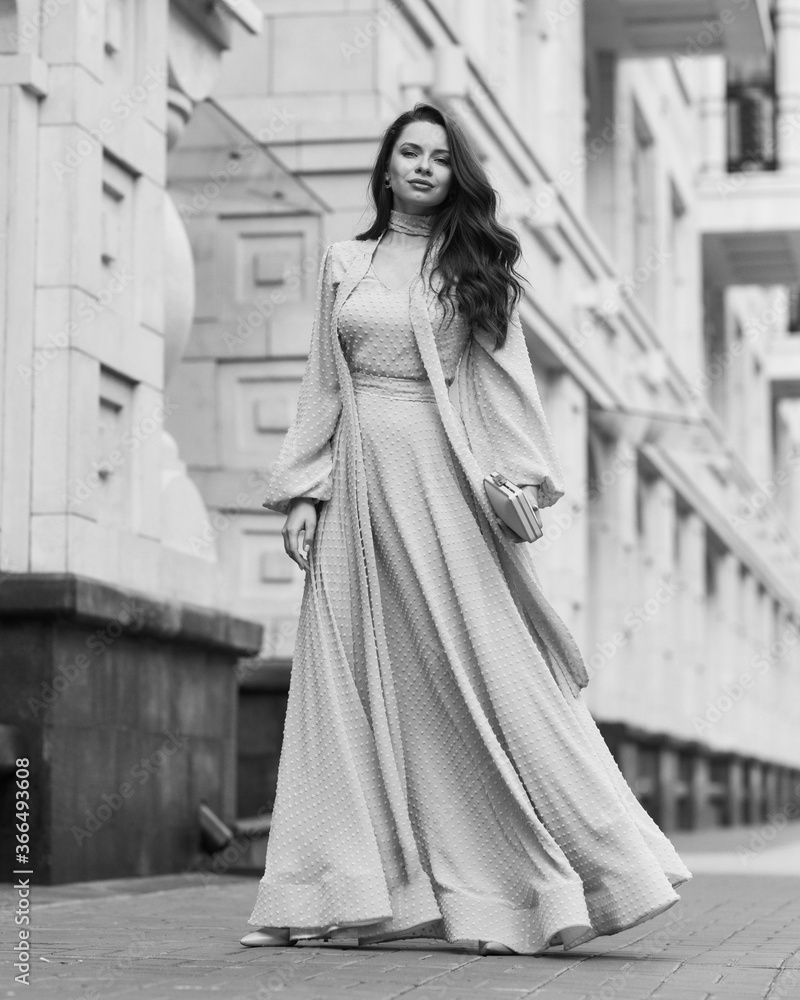 Fashion outdoor portrait. Young stylish woman in long pink evening dress walking at city street on a summer day. Full length
