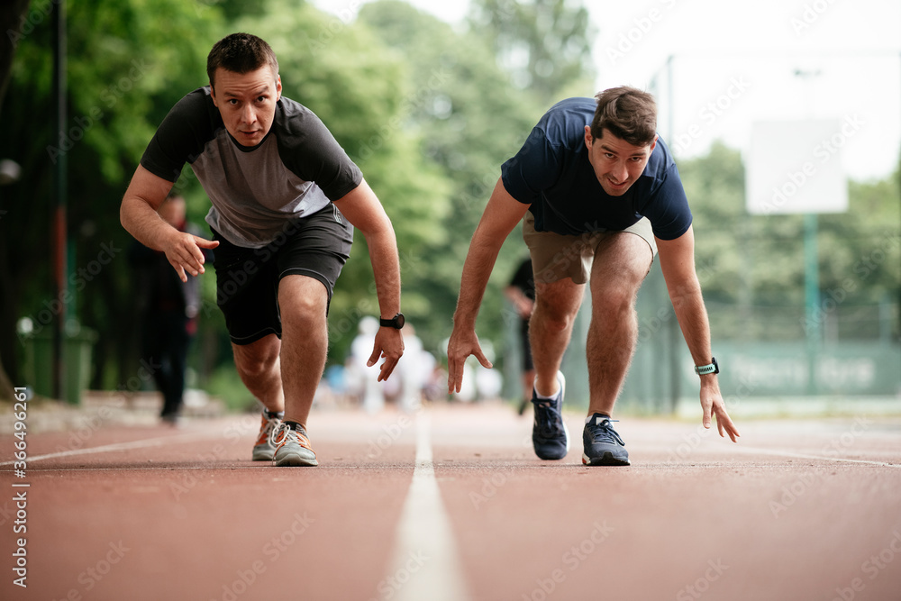 Young men training on a race track. Two young friends running on the athletics track	